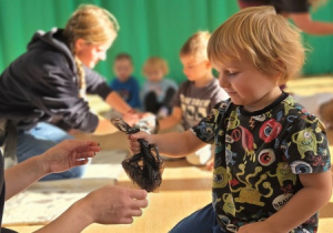 Chłopiec klęczący na podłodze przekazuje instruktorce woreczek na psie odchody.
