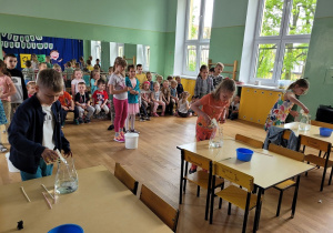 Dzieci wlewają wodę kubeczkami do dzbanków