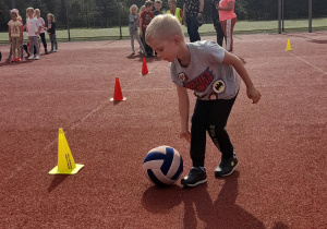 Chłopiec toczy piłkę pomiędzy pachołkami