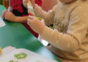 3.Dziewczynka maluje jabłko zielona farbą i robi stemple na kartce.
