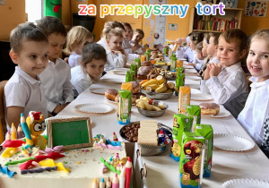 Dzieci przy stole na którym widać tort i słodycze