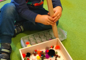 6.Chłopczyk wkłada do pojemników z otworkami kolorowe pompony przy użyciu dużej pęsety