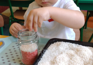 6.Chłopiec wsypuje biały ryż do słoika