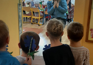 Tygryski postanowiły zrobić niespodziankę również Pani Marcie, która widać, że jest zaskoczona prezentem od Tygrysków. Dzieci wręczają jej niebieski kwiatek.