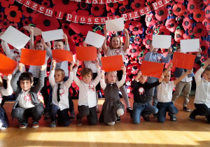 Dzieci śpiewają piosenkę, trzymając flagę Polski w górze.