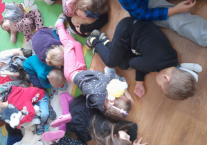 Dzieci uczestniczą w zabawie „Stary niedźwiedź” i leżą na podłodze.