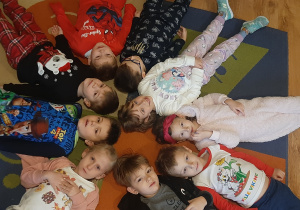 Dzieci z grupy Tygryski leżą głowami do środka koła w piżamach na dywanie.