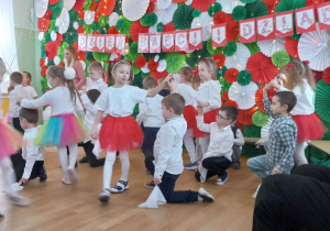 Dzieci tańczą do utworu Kawiarenki. Trzymają w rękach białe chustki.