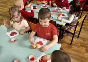 5.Dzieci siedzą przy stolikach wykonując pracę plastyczną „Serce” przy użyciu spinaczy, gąbki i farby.