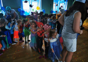 Nauczycielka jako kapitan prowadzi dzieci jedno za drugim w tanecznej zabawie.