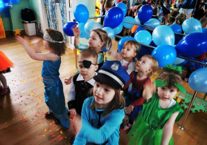 Dzieci przebrane w stroje tańczą na sali gimnastycznej w czasie balu karnawałowego