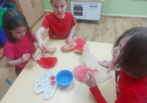 Hania, Wiktor i Julia malują walentynki tekturowe czerwoną farbą