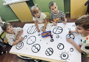 Dzieci siedzą przy stoliku i kolorują kropki