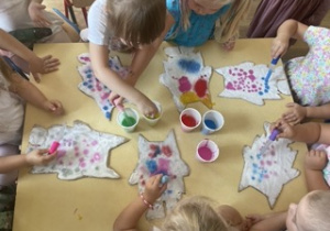 Dzieci siedzą przy stoliku nabierają kolorowej wody za pomocą pipety i kolorują sól przyklejoną do tekturowego potwora
