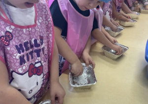 Dzieci smarują foremki do ciasta masłem.