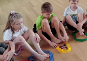 Dzieci stopami przekładają kasztany z jednej szarfy do drugiej.