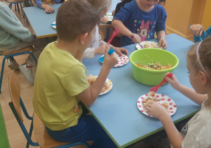 Dzieci nakładają i jedzą sałatkę.