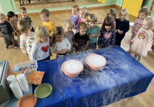 Zdjęcie dzieci stojących przy stole podczas eksperymentu z suchym lodem.