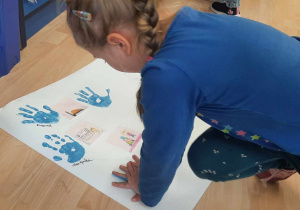 Dziewczynka z grupy Tygrysków odbija pomalowaną na niebiesko dłoń na plakacie.