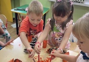 Dzieci maczają pędzle w pomarańczowej farbie i malują szyszki -ogony wiewiórek