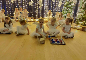 Dziewczynki siedzą w siądzie skrzyżnym przed nimi leżą dzwonki.( Instrumentacja „Little Suite from the Anna Magdalena”)