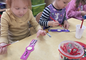 Dzieci dekorują piankowe zegarki świecącymi ozdobami.