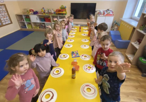 Zdjęcie grupowe dzieci stojące przy stoliku przed rozpoczęciem pracy plastycznej.