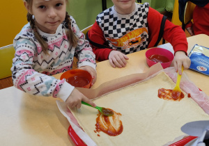 Dzieci smarują pizzę sosem pomidorowym