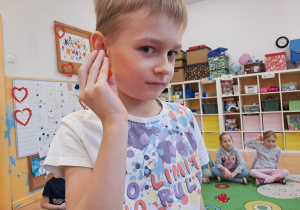 Chłopiec wykonuje zadanie "U jak ucho słyszy" - potrząsa pudełeczkiem, w którym ukryte są drobne elementy i rozpoznaje co to za przedmiot.