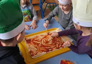 Dzieci smarują ciasto sosem pomidorowym.