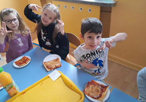Przedszkolaki szykują się do zjedzenia pizzy.
