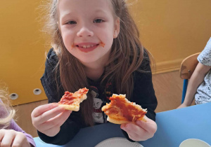 Dziewczynka ze smakiem zjada swój kawałek pizzy.