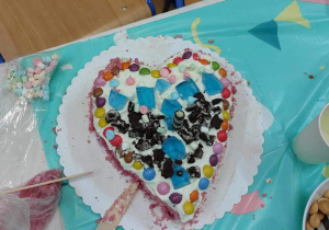 Tort w kształcie serca udekorowany galaretkami, piankami, cukierkami czekoladowymi.