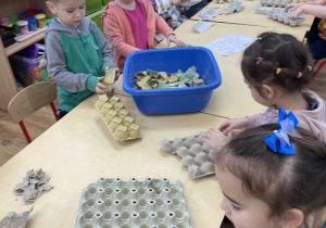 Dzieci rwą na małe kawałki tekturowe pojemniki po jajkac