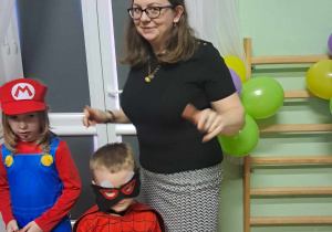 Chłopiec z stroju Maria i chłopiec Spidermana z panią przebraną za myszkę wesoło się bawią.