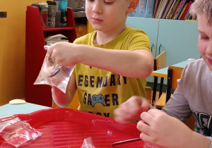 Chłopcy przekłuwają ołówkiem woreczek wypełniony wodą.