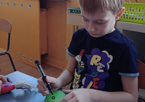 Chłopiec rysuje mazakiem oczy na swoim balonowym gniotku.