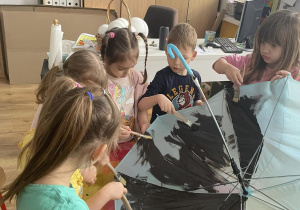 Dzieci malują czarną farbą parasol.