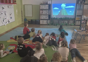 Dzieci oglądają na tablicy interaktywnej bajkę edukacyjna na temat wulkanów.