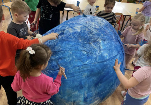 Dzieci malują niebieska farbę duży model Ziemi.