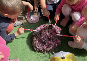 Dzieci przyklejają do modelu mrowiska igły sosny, posypują piaskiem.