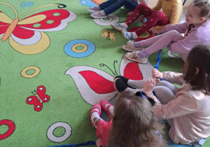 Dzieci siedzą na dywanie i bawią się przy muzyce z gumą sensoryczną.