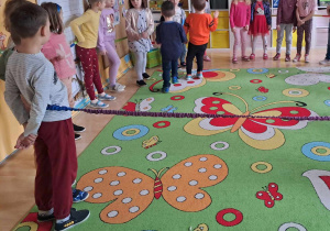 Dzieci ustawione dookoła dywanu bawią się z gumą sensoryczną.