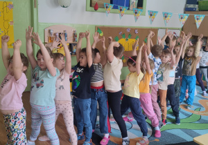 Przedszkolaki ćwiczą, trzymają ręce uniesione w górze