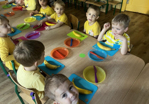 Zdjęcie przedstawiające dzieci siedzących przy stole podczas zajęć kulinarnych.