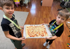 Dzieci niosą pizzę do kucharza.