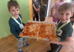 Przedszkolaki niosą pizzę.