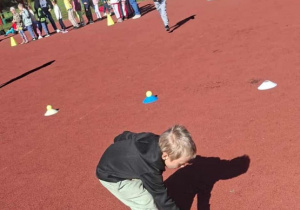 Chłopiec pochyla się, aby położyć małą piłeczkę na plastikowym pachołku podczas zawodów.