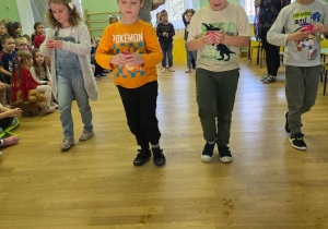 Kilkoro dzieci biegnie z kubeczkami z wodą w zabawie strażackiej.