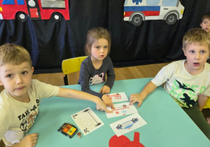 Dzieci wskazują odpowiedni pojazd służbowy po wysłuchaniu zagadki dźwiękowej.